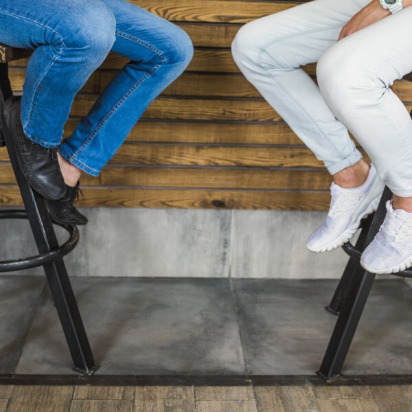Trois tabourets de bar modernes en métal noir avec dossiers courbés alignés contre une longue table commune en bois dans un cadre professionnel ou de bureau.