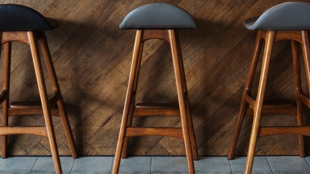 Three minimalist black metal bar stools with curved backrests arranged along a light wood breakfast bar in a bright room.