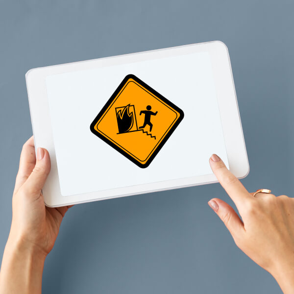Une personne tenant une tablette affichant un panneau de sécurité orange pour l'évacuation en cas d'incendie.