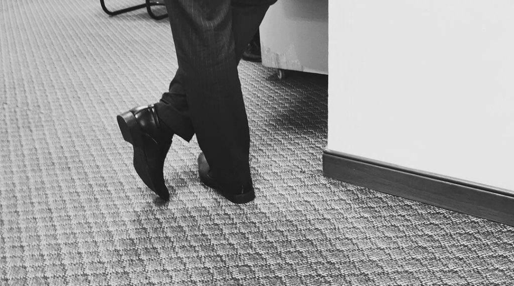 Un homme en costume se tient dans un bureau, illustrant l'importance du confort au travail avec un tapis ergonomique.